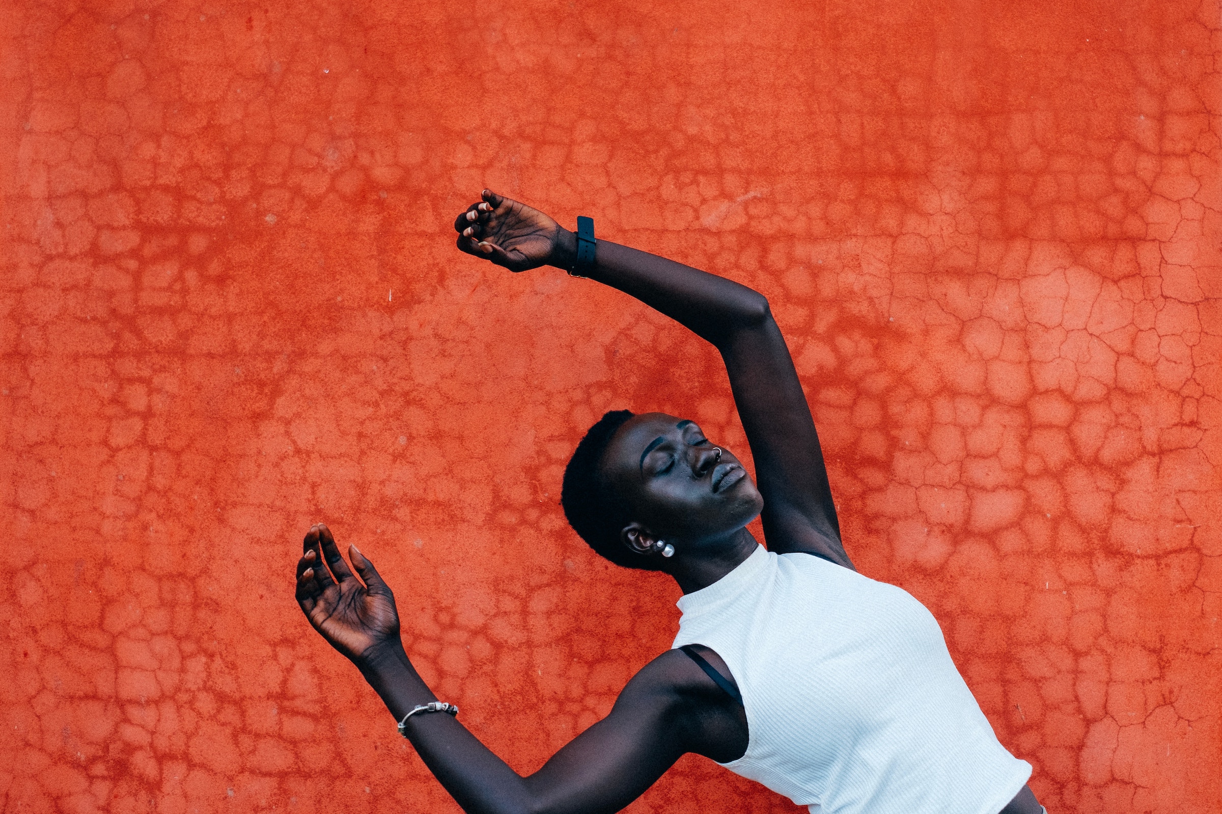 Community healing can be a powerful resource for those of us who feel isolated in a world that can feel discouraging. Young black woman appears to be in a free fall behind a red backdrop with her eyes closed. Her facial expression is neutral.